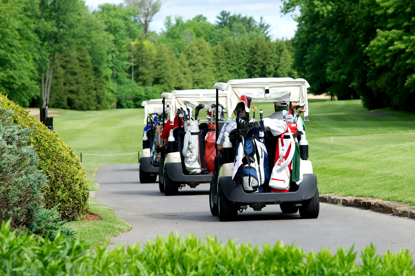 Line of Three Golf Carts Driving on a Road Beside the Course